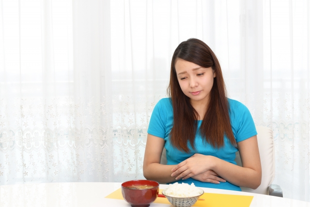 食事を前にして胃の不調が気になる女性